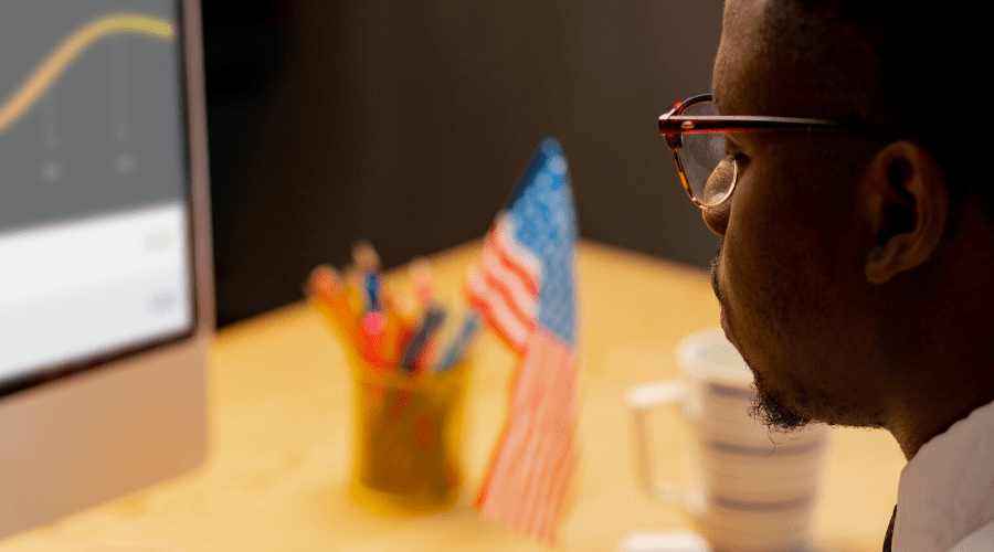 Concept photo of a man looking intently at a computer with a small American flag in the background.