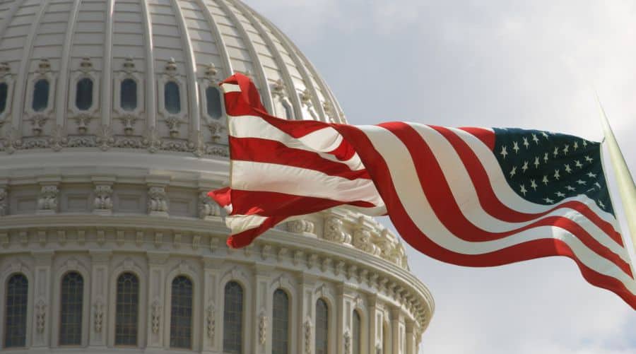 Photo of the American flag waving in the wind with the Capitol in the background.